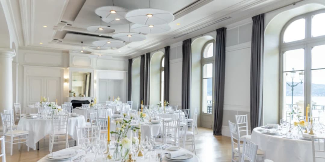 Brightly lit restaurant with large round tables set up for a wedding, Abstracta lily light acoustic panels hang from the ceiling improving the acoustics