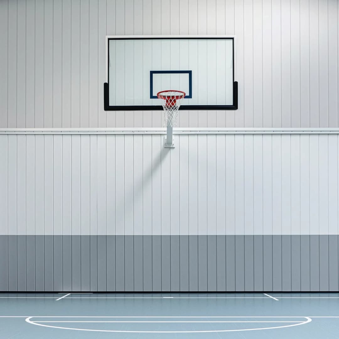 view of a sports hall wall with high level acoustic panelling behind a basketball hoop. The space is well lit with neutral grey colours