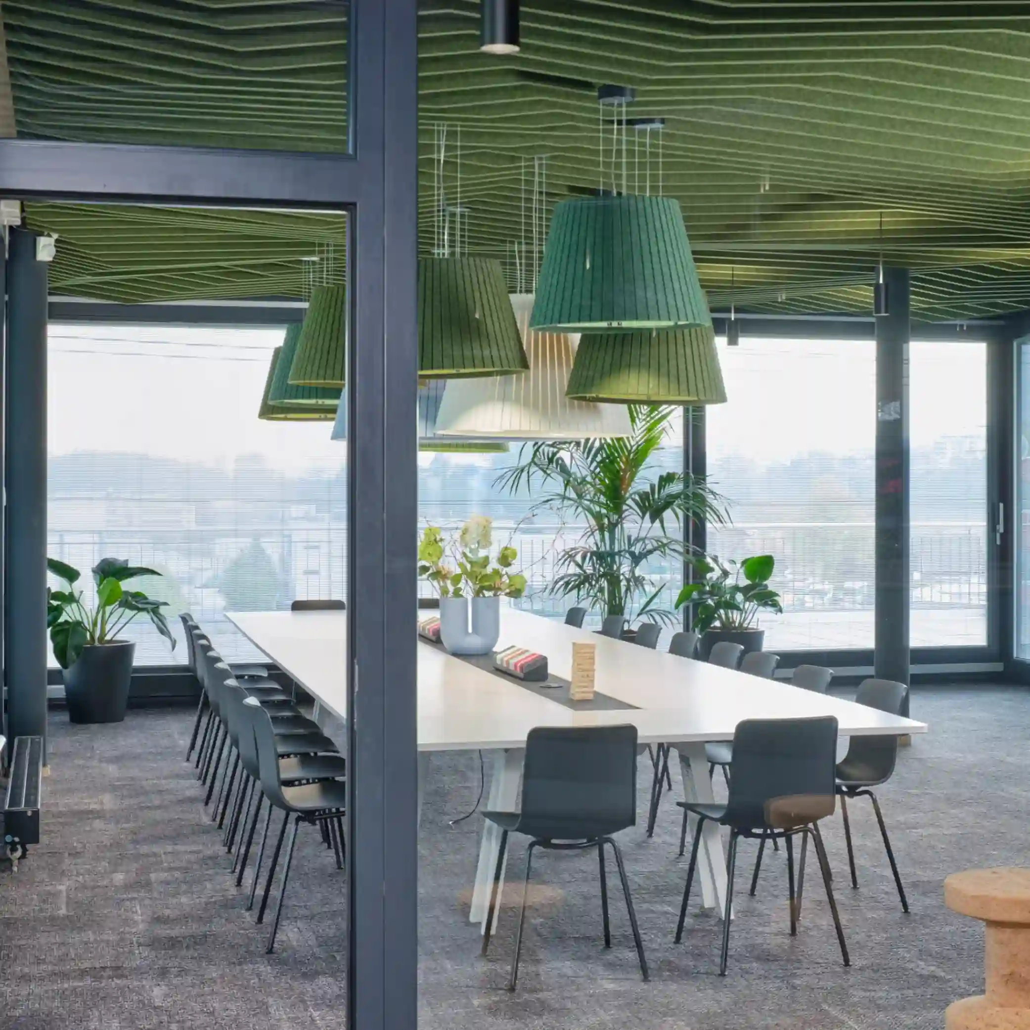 looking through glass partition to a meeting room with green acoustic baffles covering the ceiling and acoustic pendant lights above the table