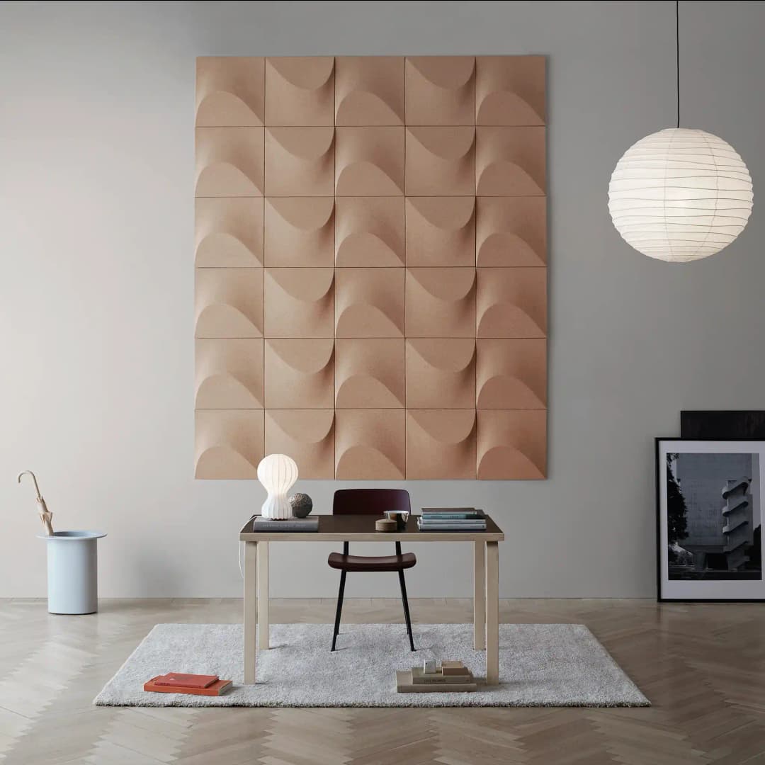 bright and airy room with small working table and scattered belongings. On the back wall are Sahara cork acoustic wall panels that mimic dunes