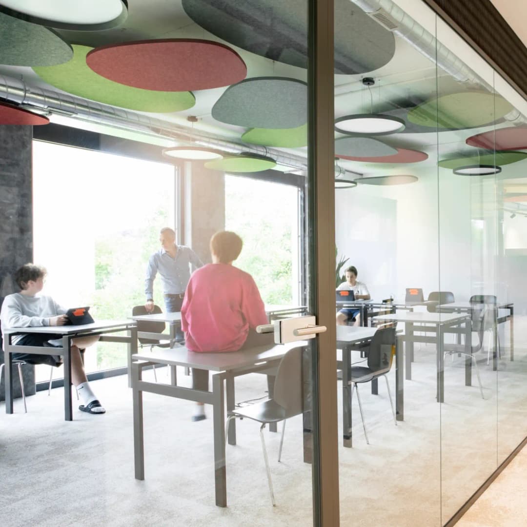pebble shaped felt acoustic ceiling rafts in green, red and grey suspended in a small school classroom. children sat at education desks