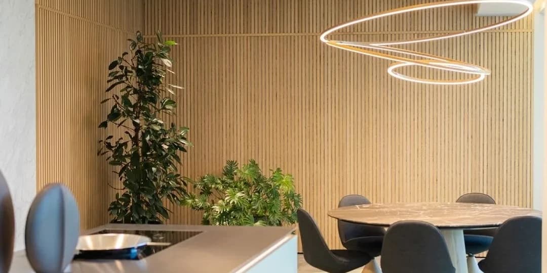 wide angle view of a domestic kitchen with round dining table and plants in the corner. on the wall are vertical slats of an oak acoustic panel system