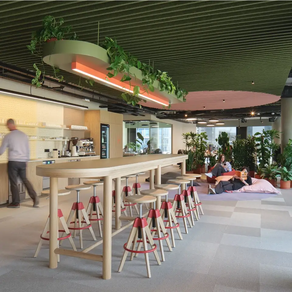 breakout area in office with a high table and stools as well as bean bags in the library section. Green baffle acoustic ceiling with feature pink circle