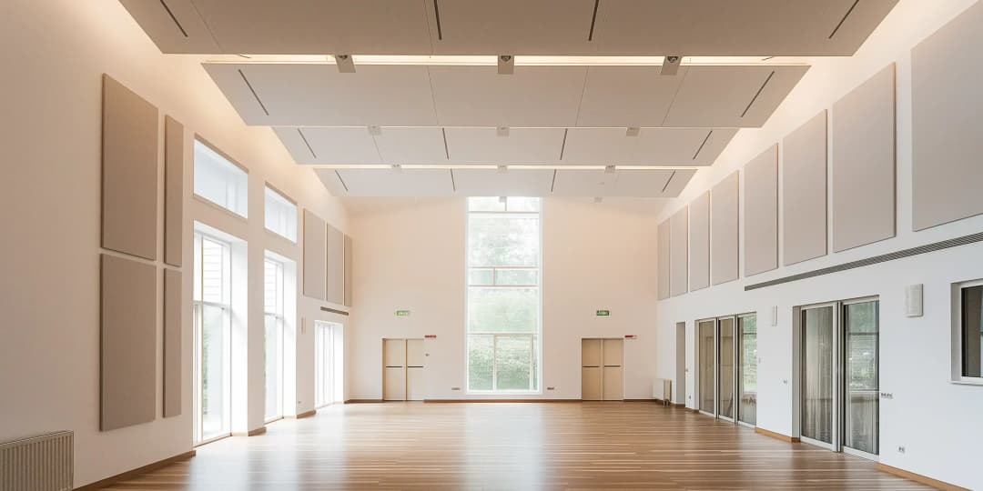 village community hall with high ceilings and wood floors. There are large acoustic panels fixed to the walls to absorb noise