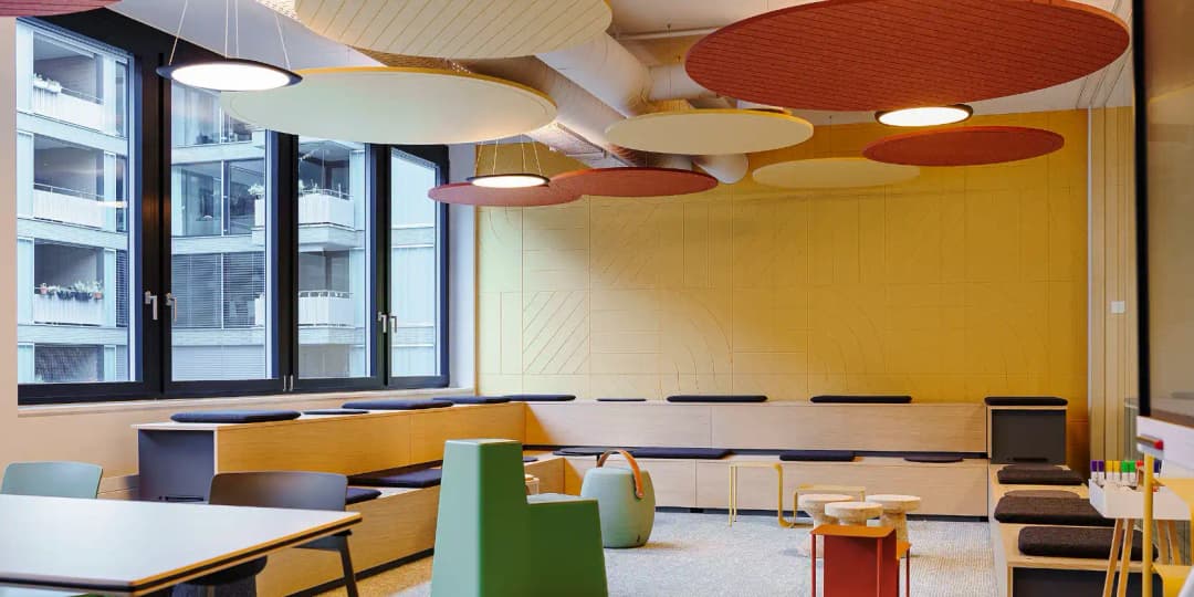 colourful classroom with tiered seating and circular acoustic ceiling rafts to improve learning in education settings
