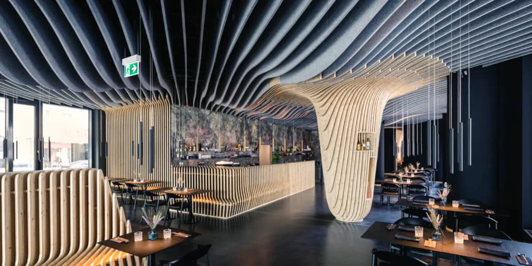 modern restaurant and bar with dark floors and bespoke wavey acoustic baffles on the ceiling that flow in to a pillar, improving the acoustics