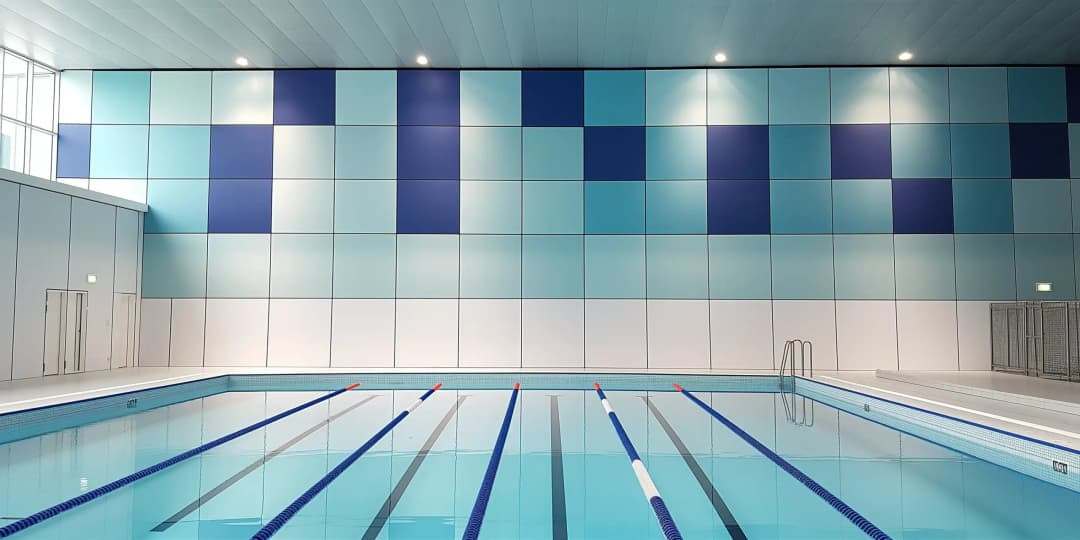 indoor swimming pool at a sports centre. tiled floor and large square acoustic wall panels installed at high level to absorb reverberation