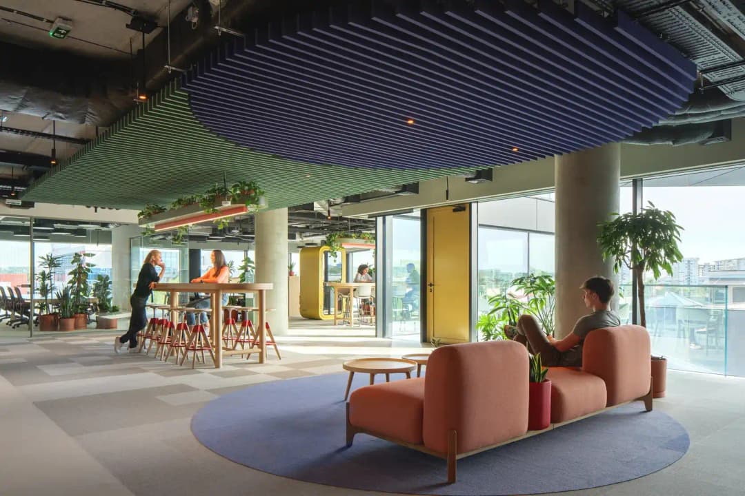 open plan office break out area with high tables and a sofa. on the ceiling are custom acoustic baffles in circular formation